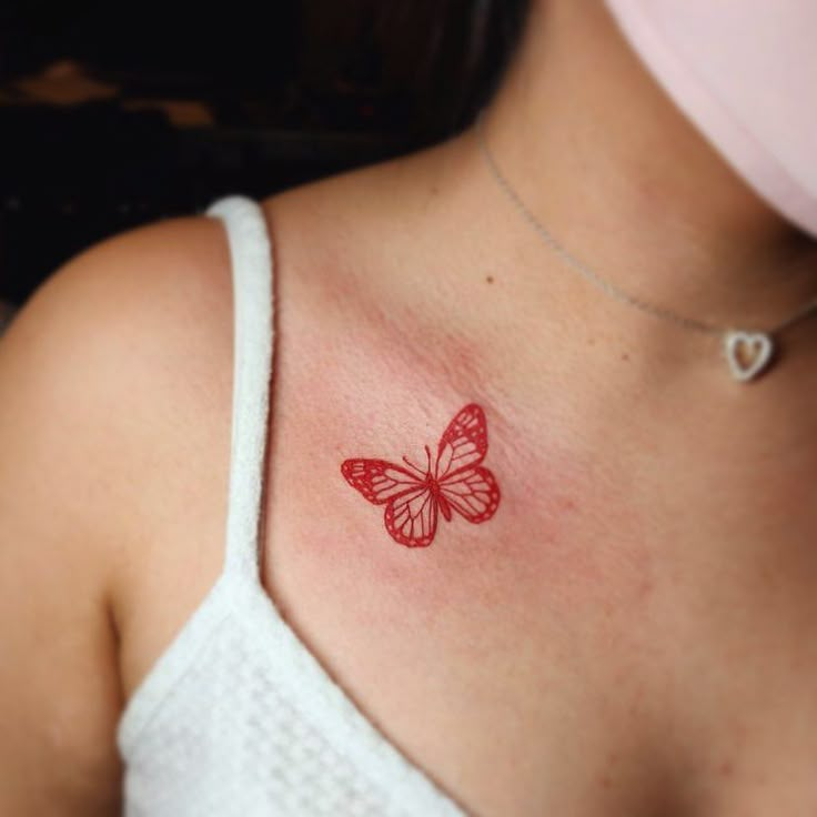 a woman's chest with a red butterfly tattoo on the left side of her neck