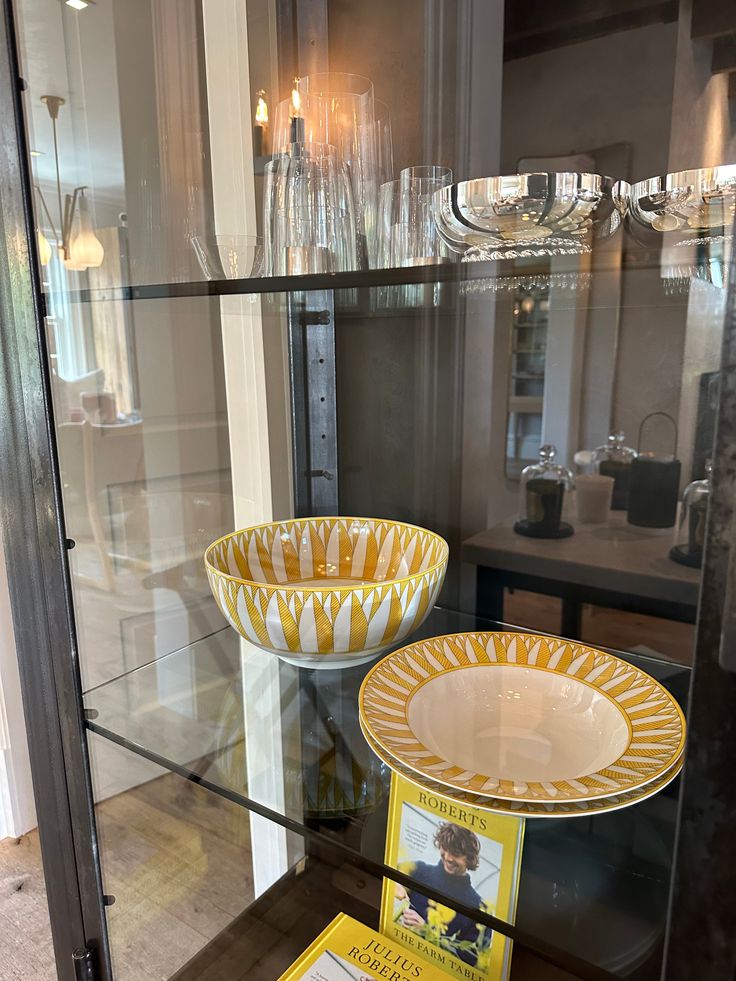 two yellow and white bowls sitting on top of a glass shelf next to each other