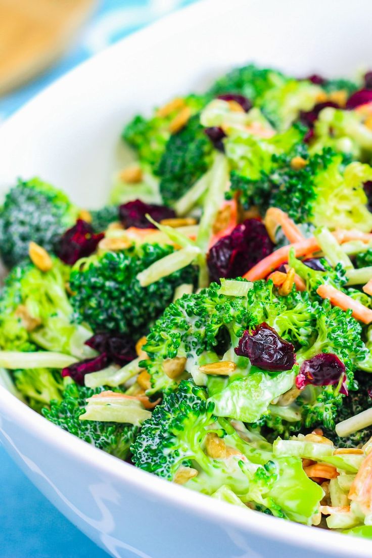 a white bowl filled with broccoli and cranberries on top of a blue table