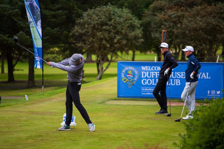 a man swinging a golf club on top of a green field