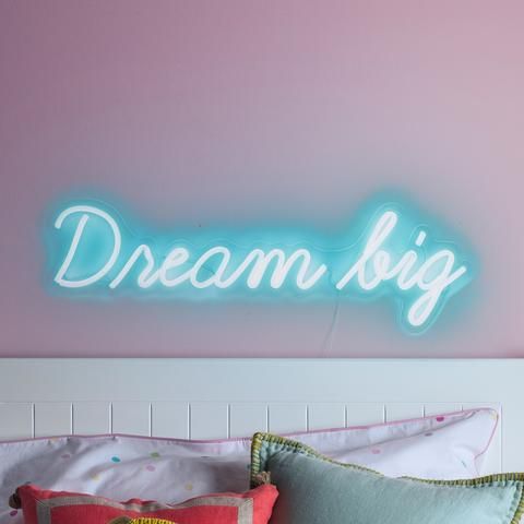 a neon sign that says dream big on the wall above a bed with two pillows