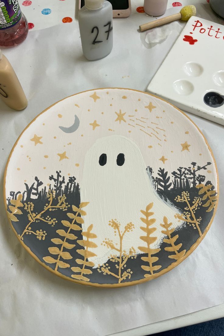 a plate with a ghost painted on it sitting on a table next to paintbrushes