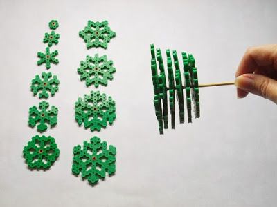 a hand holding a toothpick with green beads on it next to several smaller ones