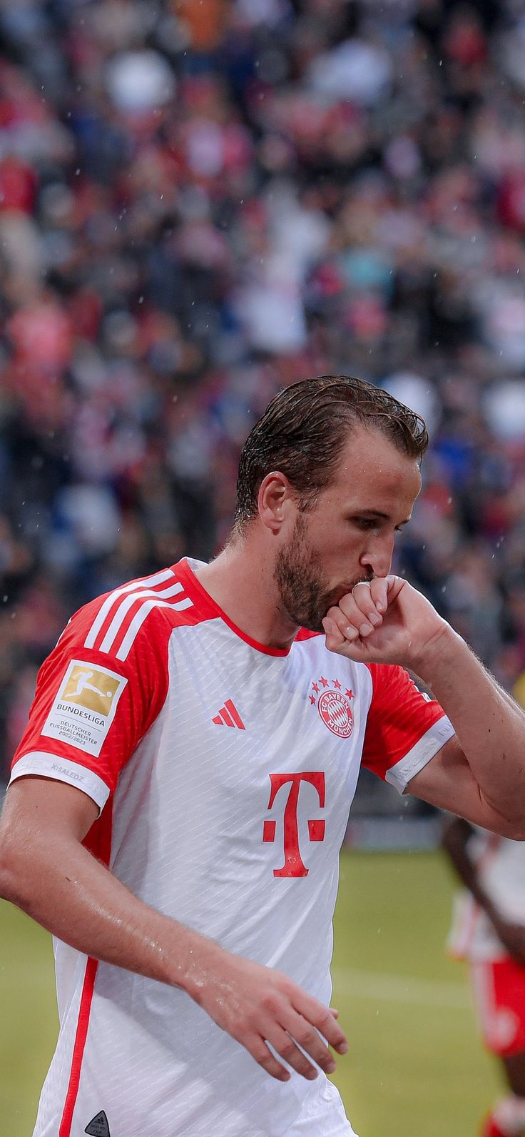 a man standing on top of a soccer field holding his hand to his mouth while wearing a red and white uniform