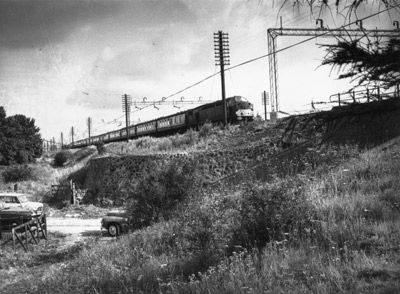 an old photo of a train going down the tracks in black and white, with power lines above it