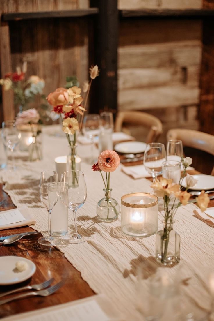 the table is set with flowers in vases and place settings for two people to sit at