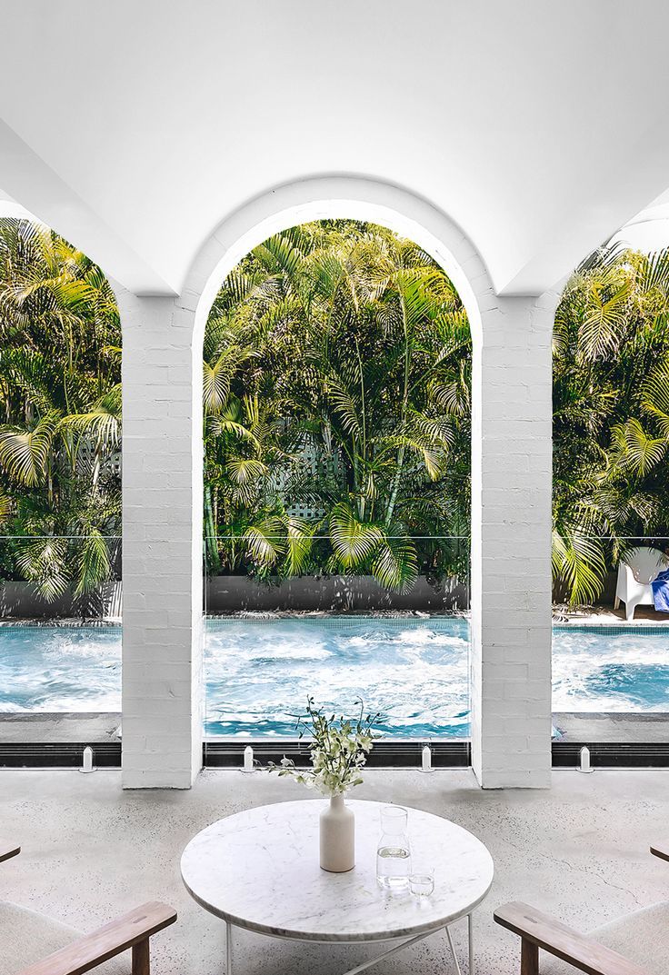 an indoor swimming pool is seen through three arched windows, with chairs around the table