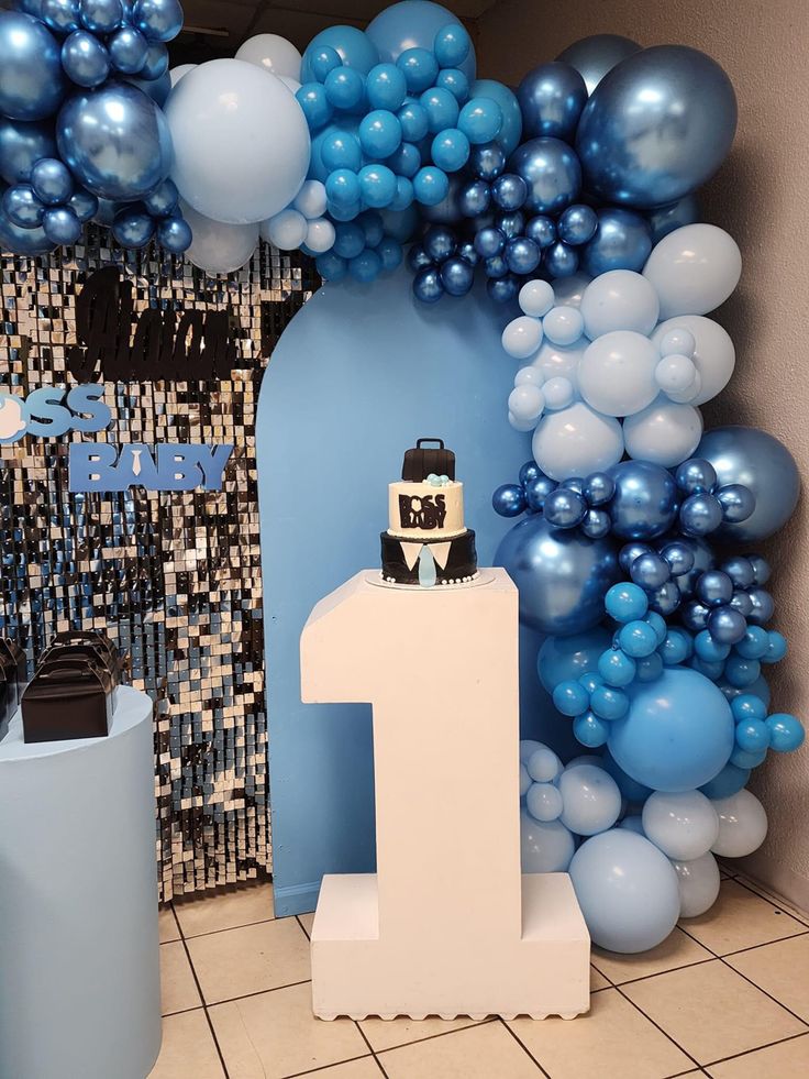 a blue and white balloon arch with a cake in the middle for a first birthday