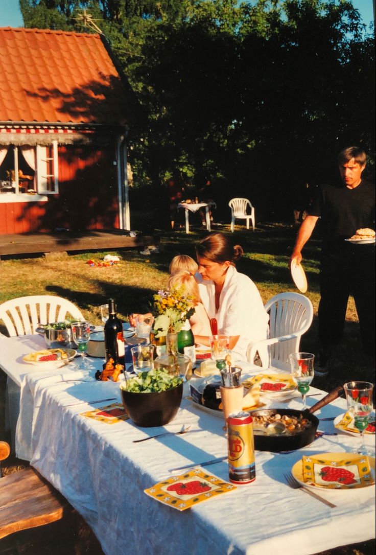 two people sitting at a table with food and drinks in front of them on the grass