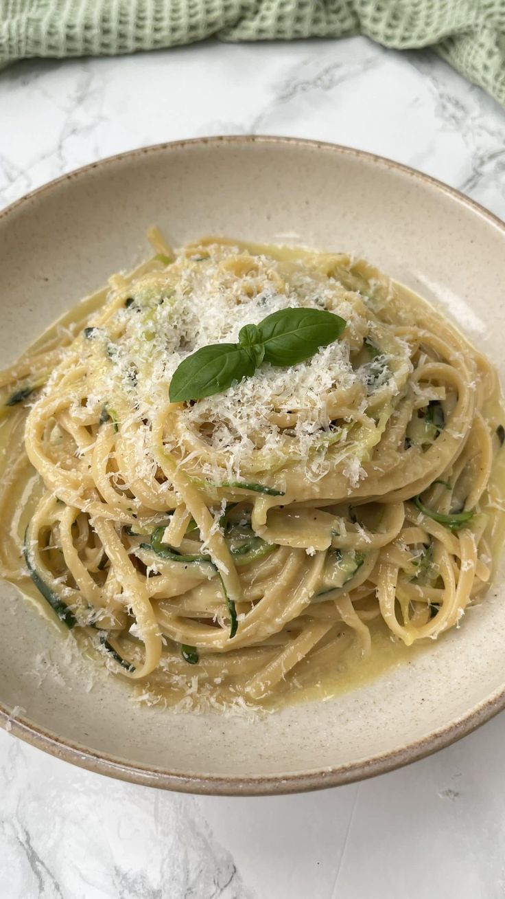 pasta with spinach and parmesan cheese in a white bowl on a marble table