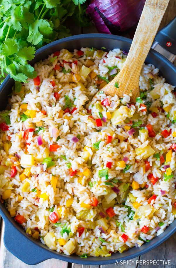 rice and vegetables are mixed together in a skillet with a wooden spoon on the side