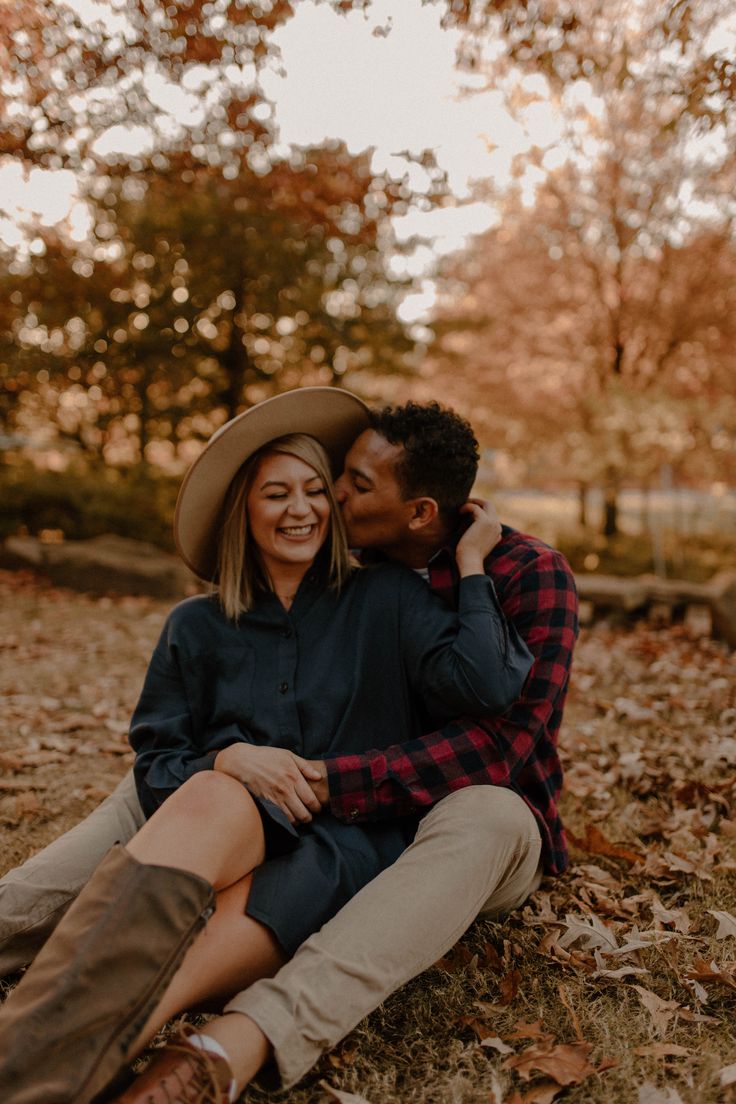 a man and woman are sitting on the ground in autumn leaves, smiling at each other