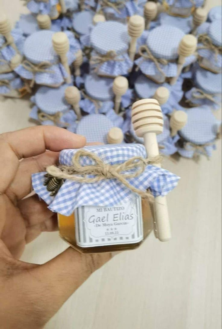 a hand holding a jar of honey next to a bunch of blue bonnets on top of a table