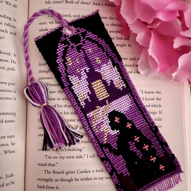 an open book with a purple beaded bookmark and pink flowers next to it