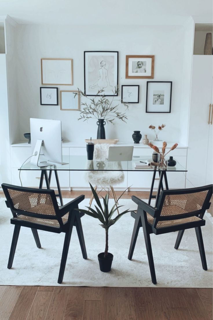 a glass table with two chairs in front of it and pictures on the wall behind it