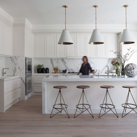 a large kitchen with white cabinets and marble counter tops, an island in the middle is flanked by three stools