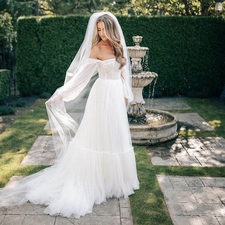 a woman in a white wedding dress standing next to a fountain and wearing a veil