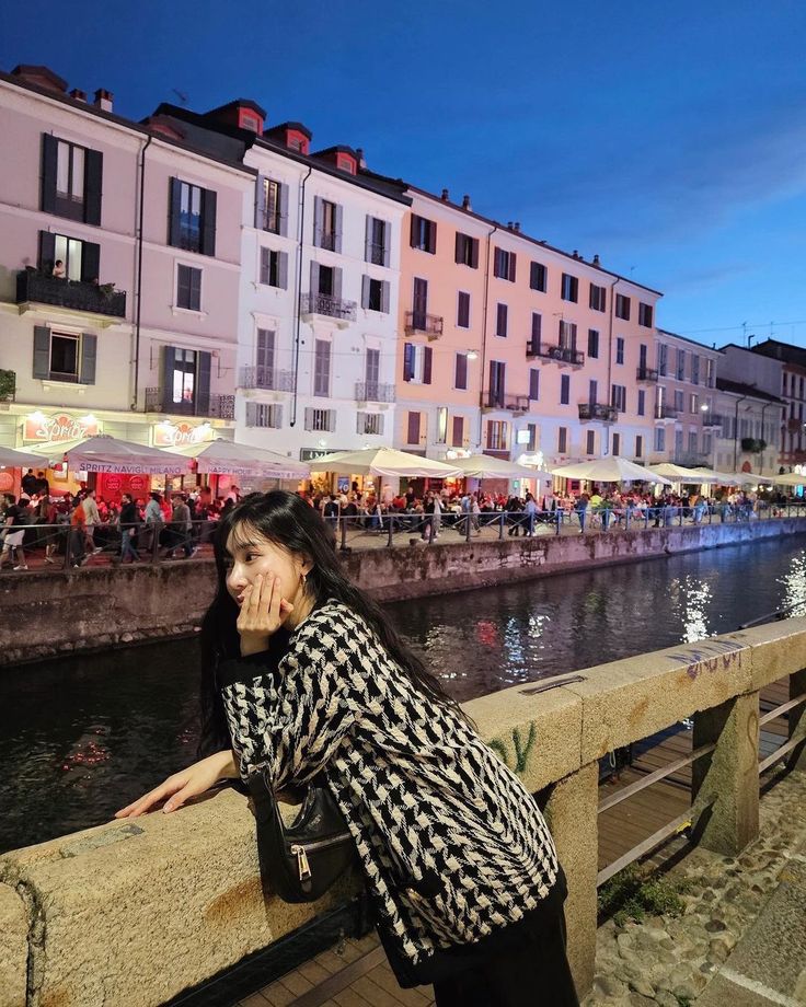 a woman leaning on a wall next to a body of water with buildings in the background