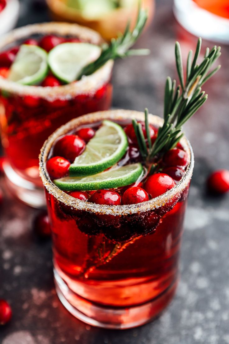 two glasses filled with cranberry margaritas and garnished with fresh herbs