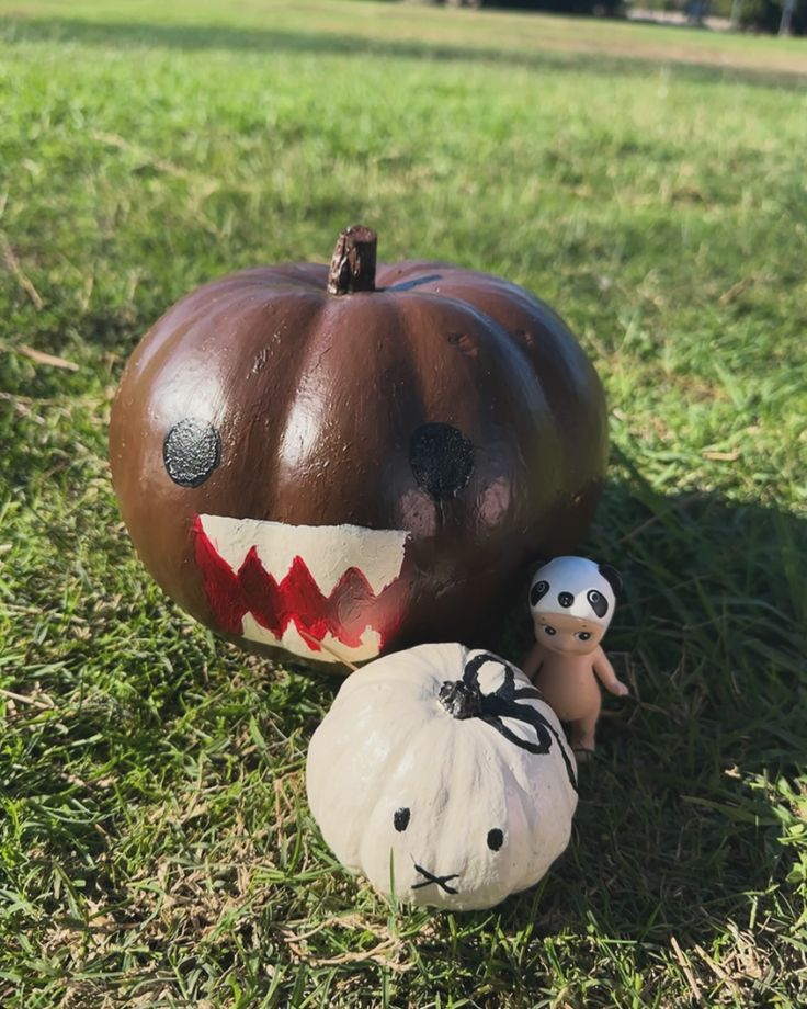 two pumpkins with faces painted on them sitting in the grass next to one another