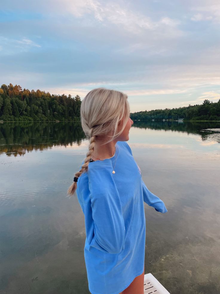 a woman standing on the edge of a boat looking out at water with trees in the background