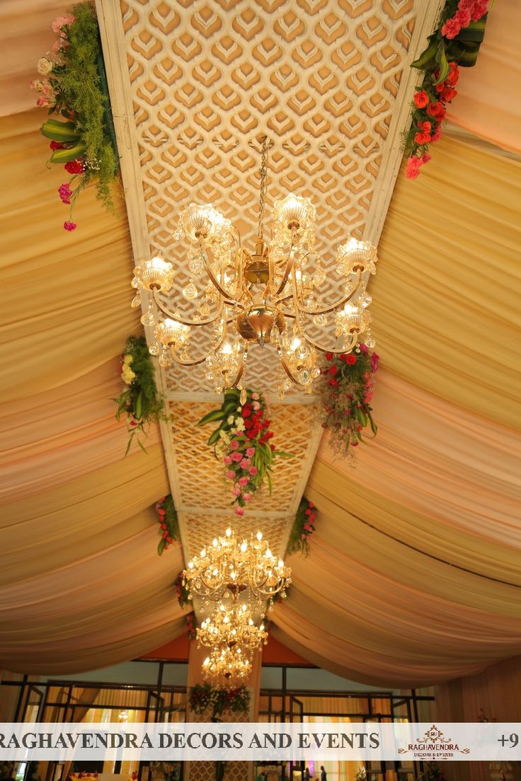 a chandelier hanging from the ceiling with flowers and greenery on it's sides