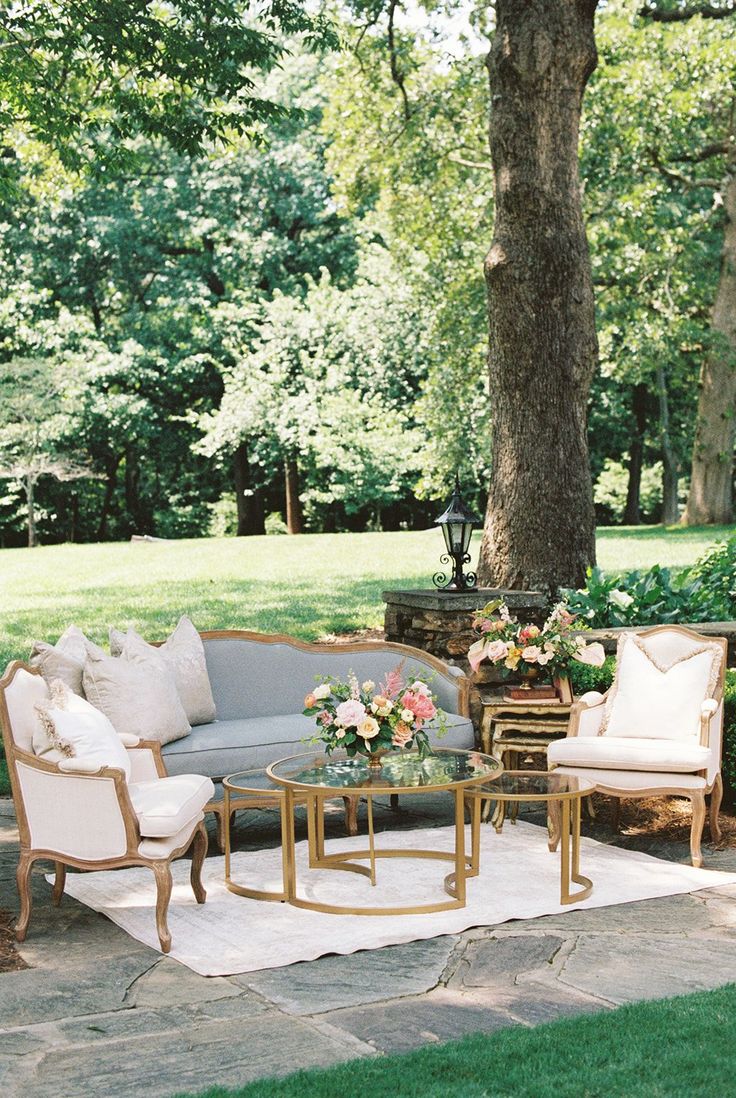 an outdoor seating area with couches, tables and chairs under a tree in the background