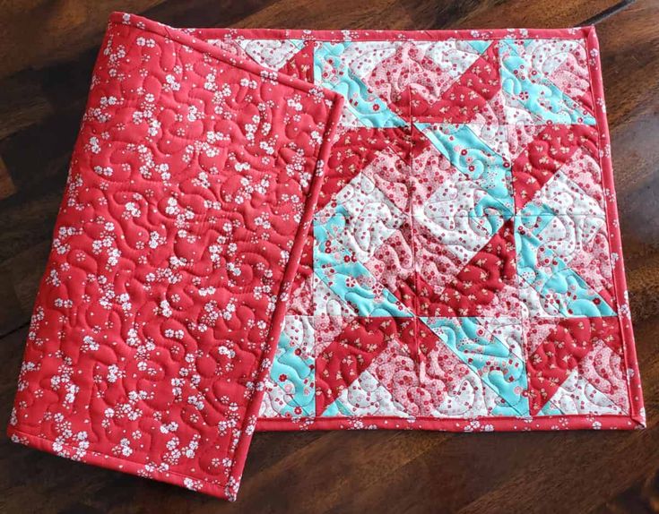 two red and white quilts sitting on top of a wooden floor next to each other