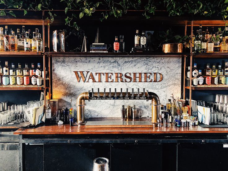 a bar with lots of bottles and glasses on top of it, next to a sign that reads watershed