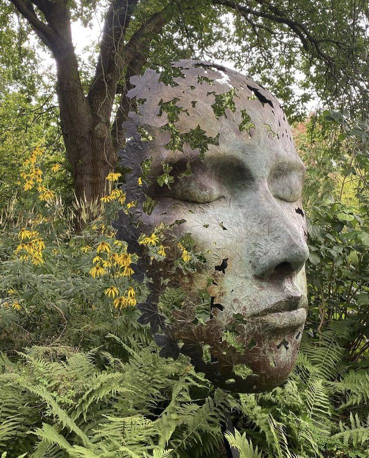 a statue is in the middle of some plants and trees with yellow flowers around it