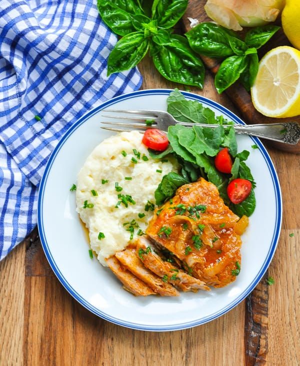 a white plate topped with meat, mashed potatoes and spinach next to lemon wedges