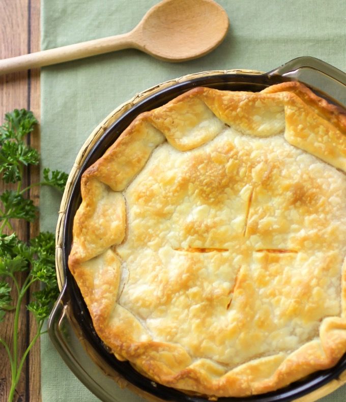 a chicken pot pie in a pan with a wooden spoon and parsley on the side