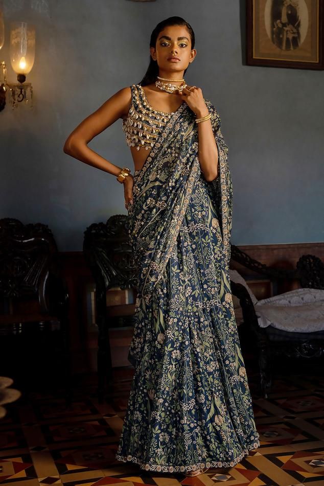 Navy blue georgette pre-draped saree with all over tropical print, metallic marodi, sequin, bead embroidered highlights and attached draped pallu. Paired with round neck padded blouse with layered kowri shells and sequin tassel details.
Components: 2
Pattern: Printed and Embellished
Type Of Work: Tropical Print, Marodi, Kowri Shell, Beads and Sequin Work
Neckline: Round Neck
Sleeve Type: Sleeveless
Fabric: Saree: Georgette, Blouse: Cotton Silk
Color: Blue
Other Details: 
Karigari time: 171 hrs
E Shell Blouse Indian, Kaudi Shell Blouse, Brownie Outfits, Sabyasachi Sarees Blouse, Marodi Work, Paulmi And Harsh, Navy Blue Saree, Saree Georgette, Draped Saree