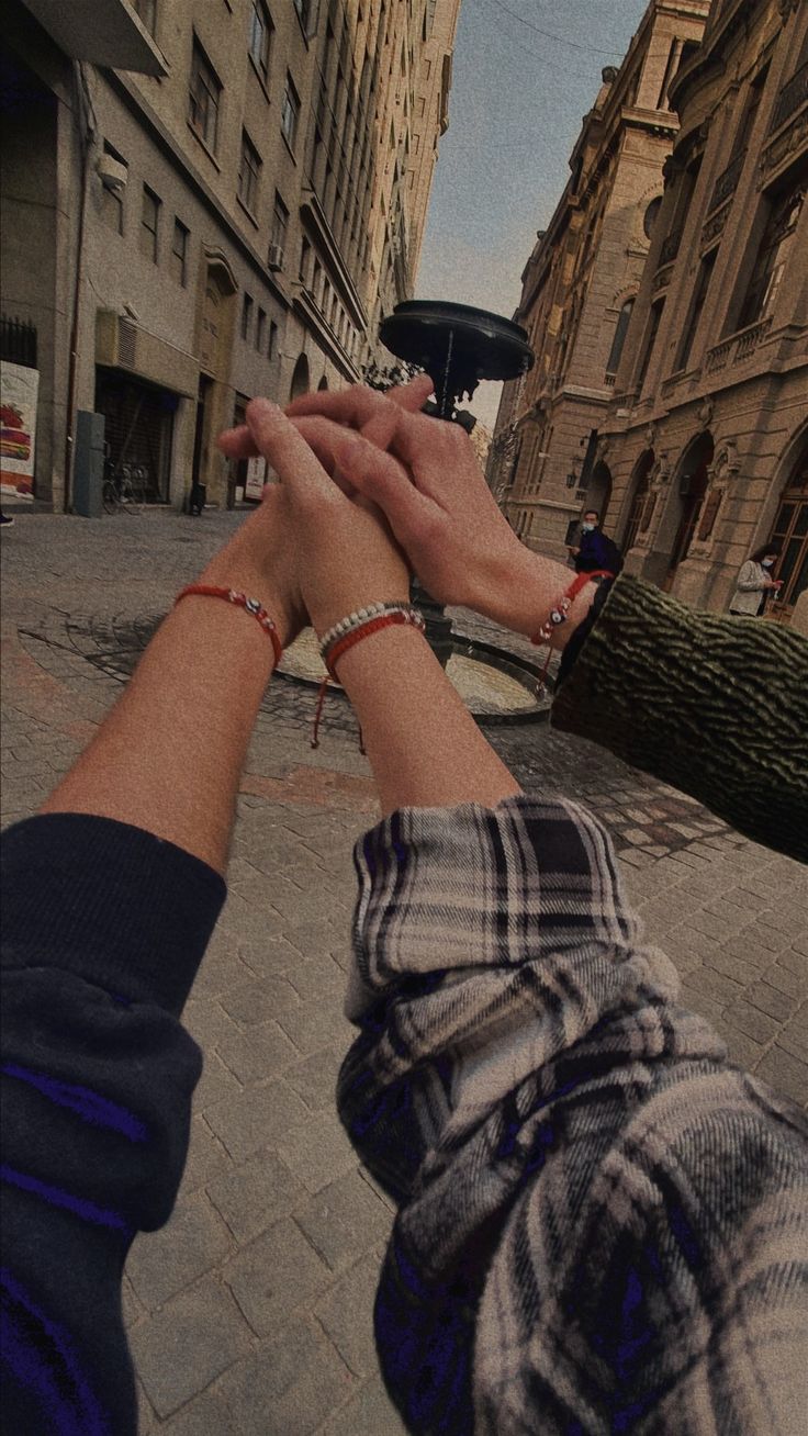 two people are holding hands in the middle of a street with buildings on both sides