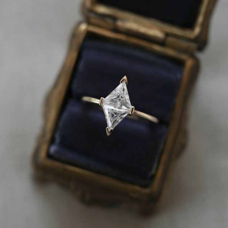 an engagement ring with a princess cut diamond sits in a box on a table top