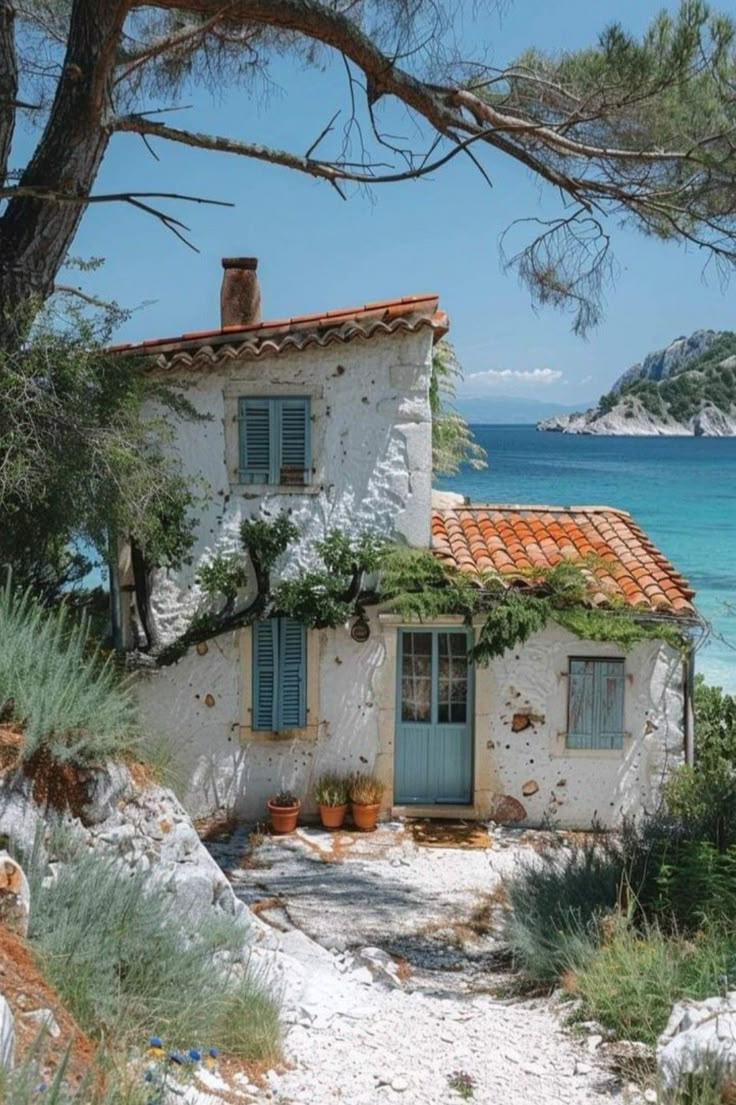 an old white house sitting on top of a sandy beach next to the ocean and trees