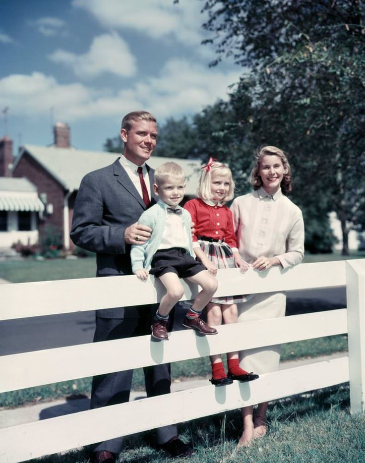 a man and two children are sitting on a white fence with their father standing next to them