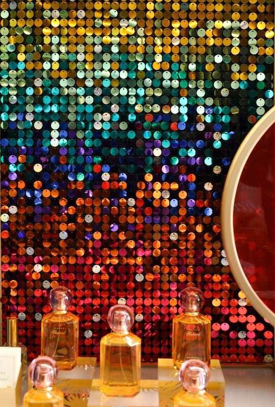 three bottles of perfume sitting on top of a table next to a mirror with colorful lights in the background