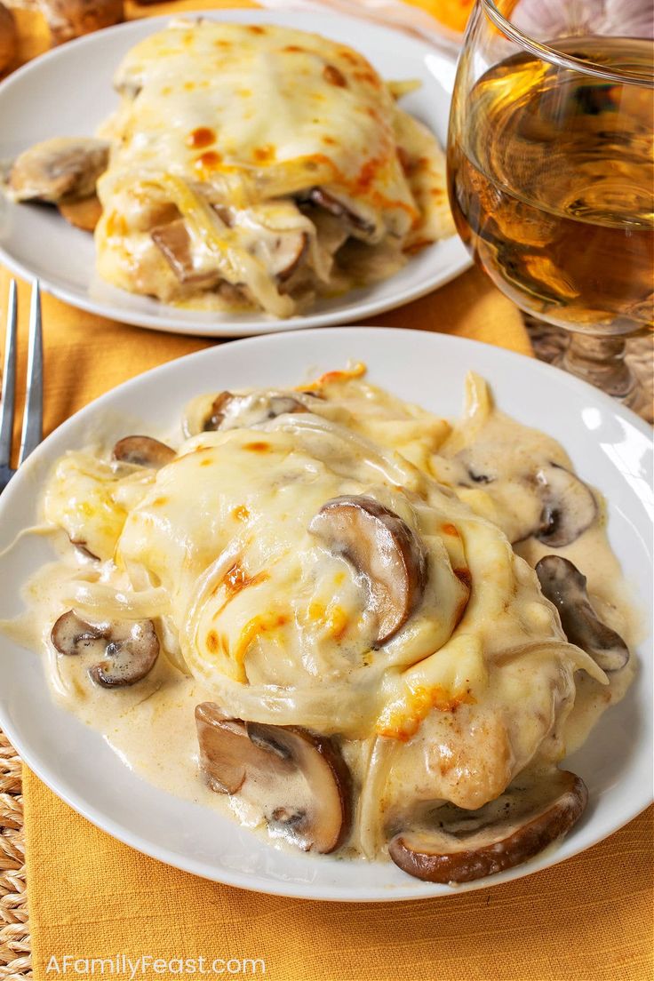 two white plates topped with pasta covered in cheese and mushrooms next to a glass of wine