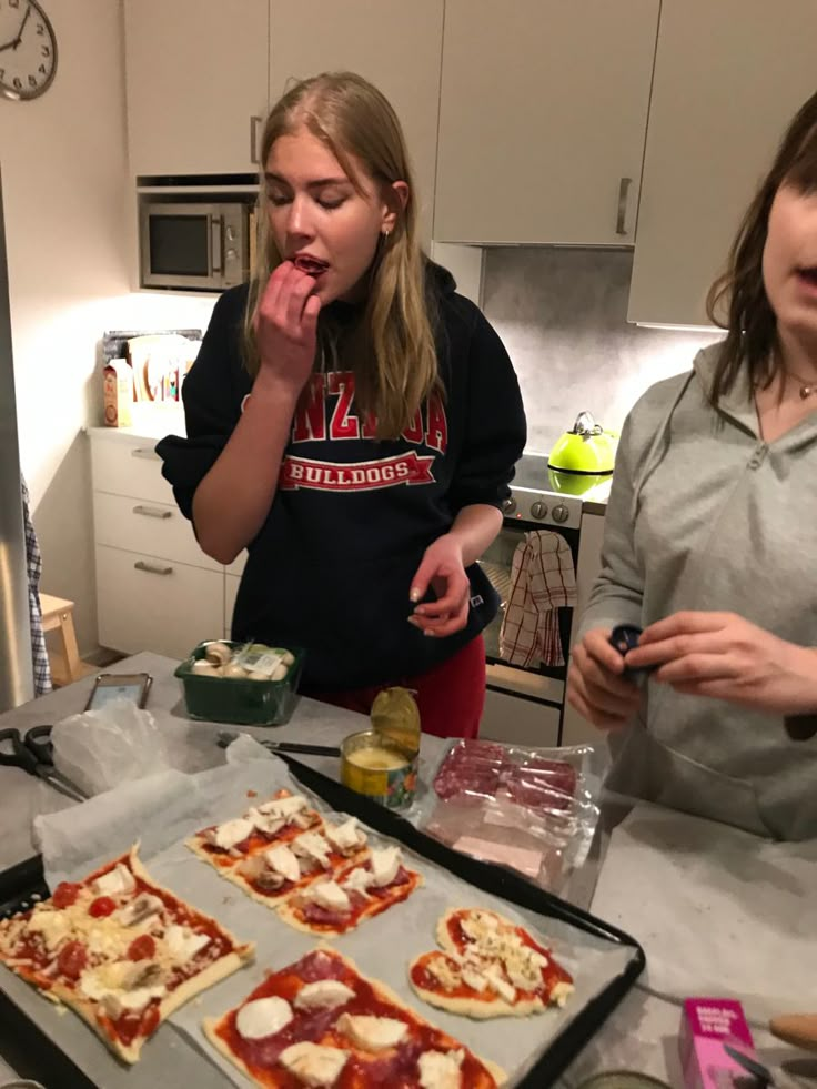 two girls are making pizzas in the kitchen