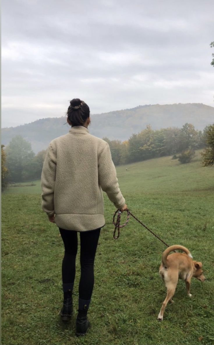 a woman walking her dog on a leash in a field with mountains in the background