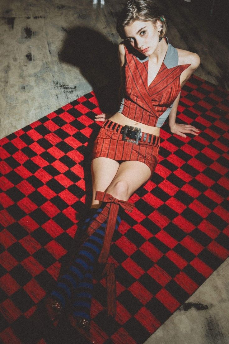 a young woman sitting on top of a red and black checkered rug with her legs crossed