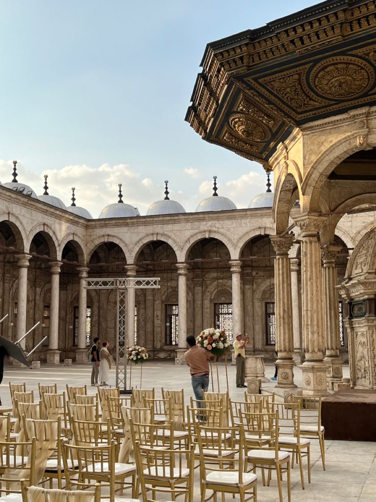 an outdoor area with many chairs and people walking around it, in the middle of a courtyard