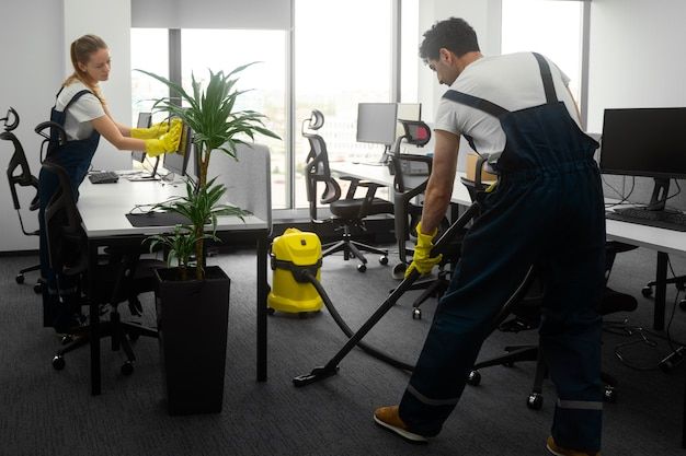 a man and woman in an office cleaning the floor with yellow vacuum mop's