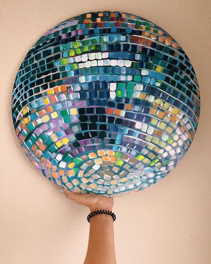 a hand is holding up a colorful mosaic glass plate on the wall above it's head