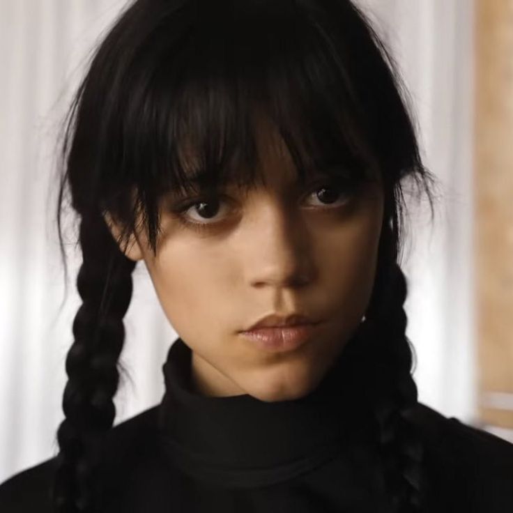 a woman with black hair and braids looks at the camera while wearing a black turtle neck sweater