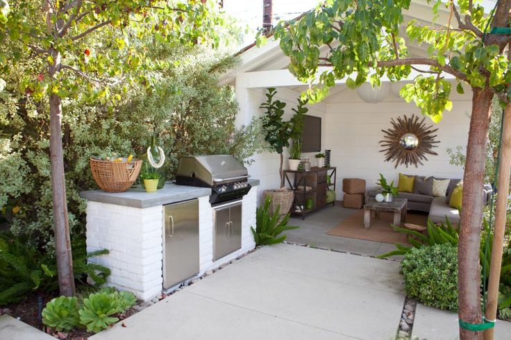 an outdoor kitchen with grill and seating area in the back yard, surrounded by greenery