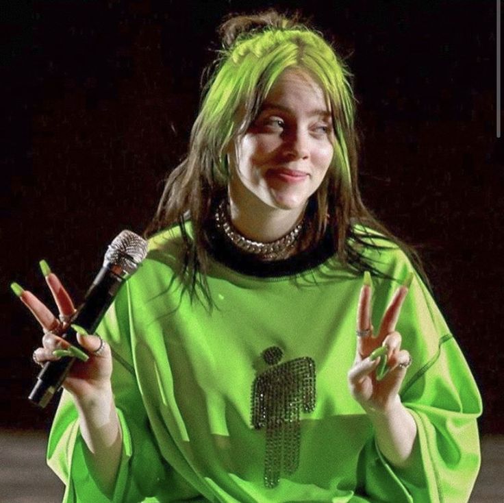 a woman with green hair is holding up two fingers and making the peace sign in front of her