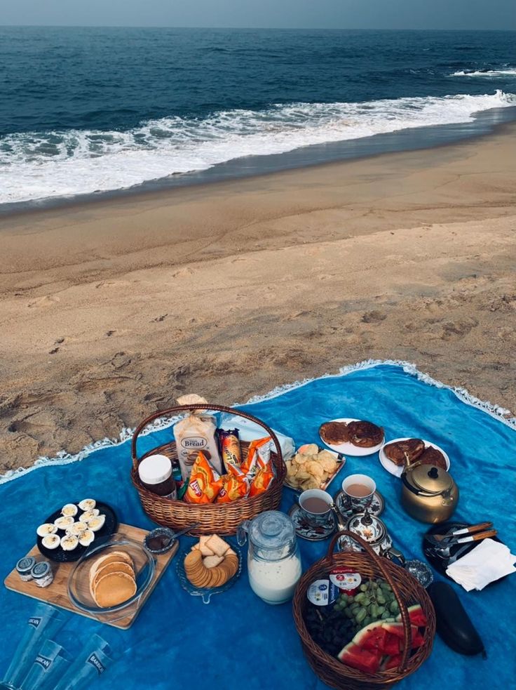 a picnic is set up on the beach with food and drinks in front of the ocean