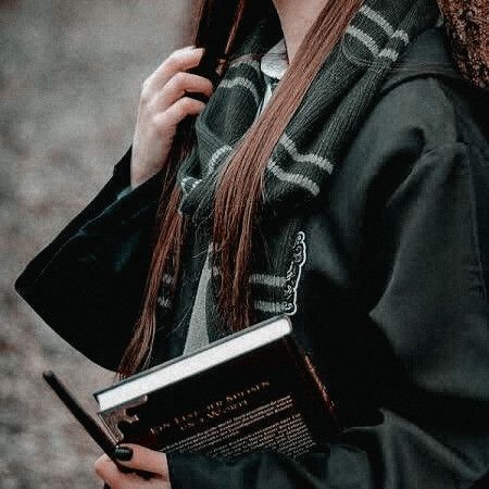 a woman with long brown hair is holding a book and looking at the camera while standing outside